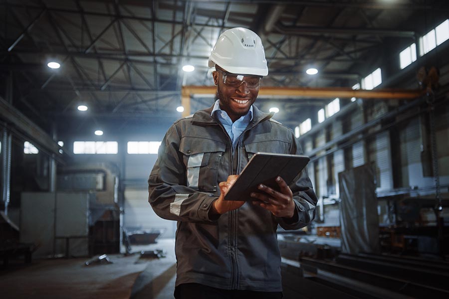 Client Center - Construction Engineer Smiling and Using a Tablet in a Warehouse, Hard Hat On